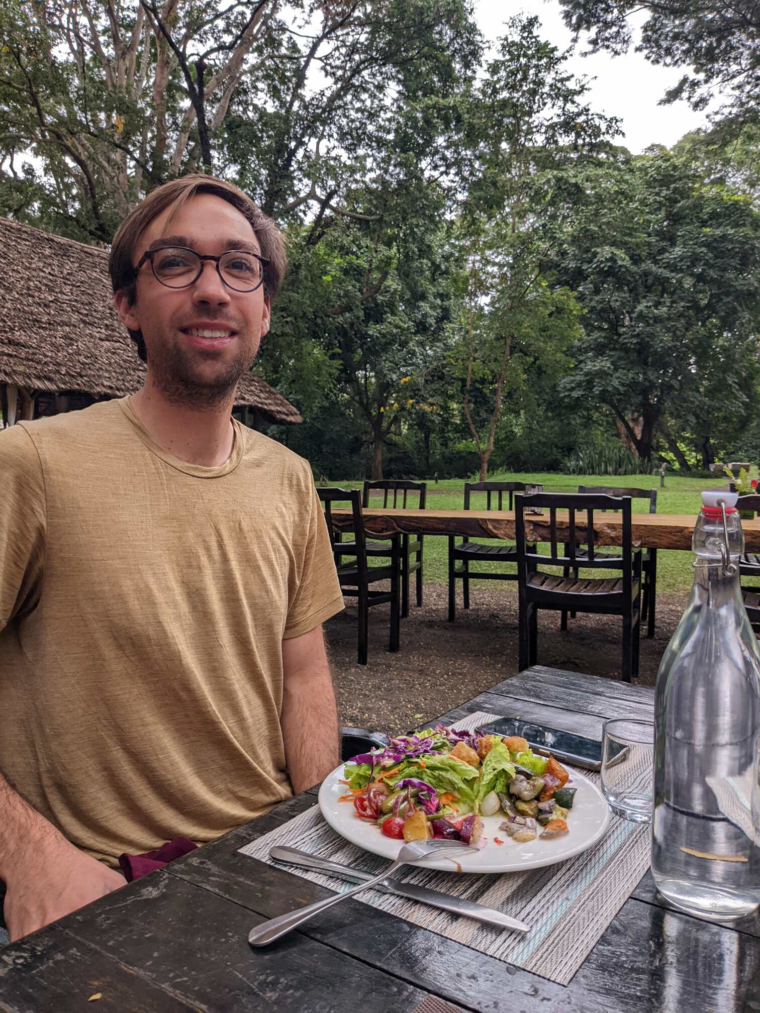 Tim eating a salad at a table outside doing his best to try and smile with chapped lips