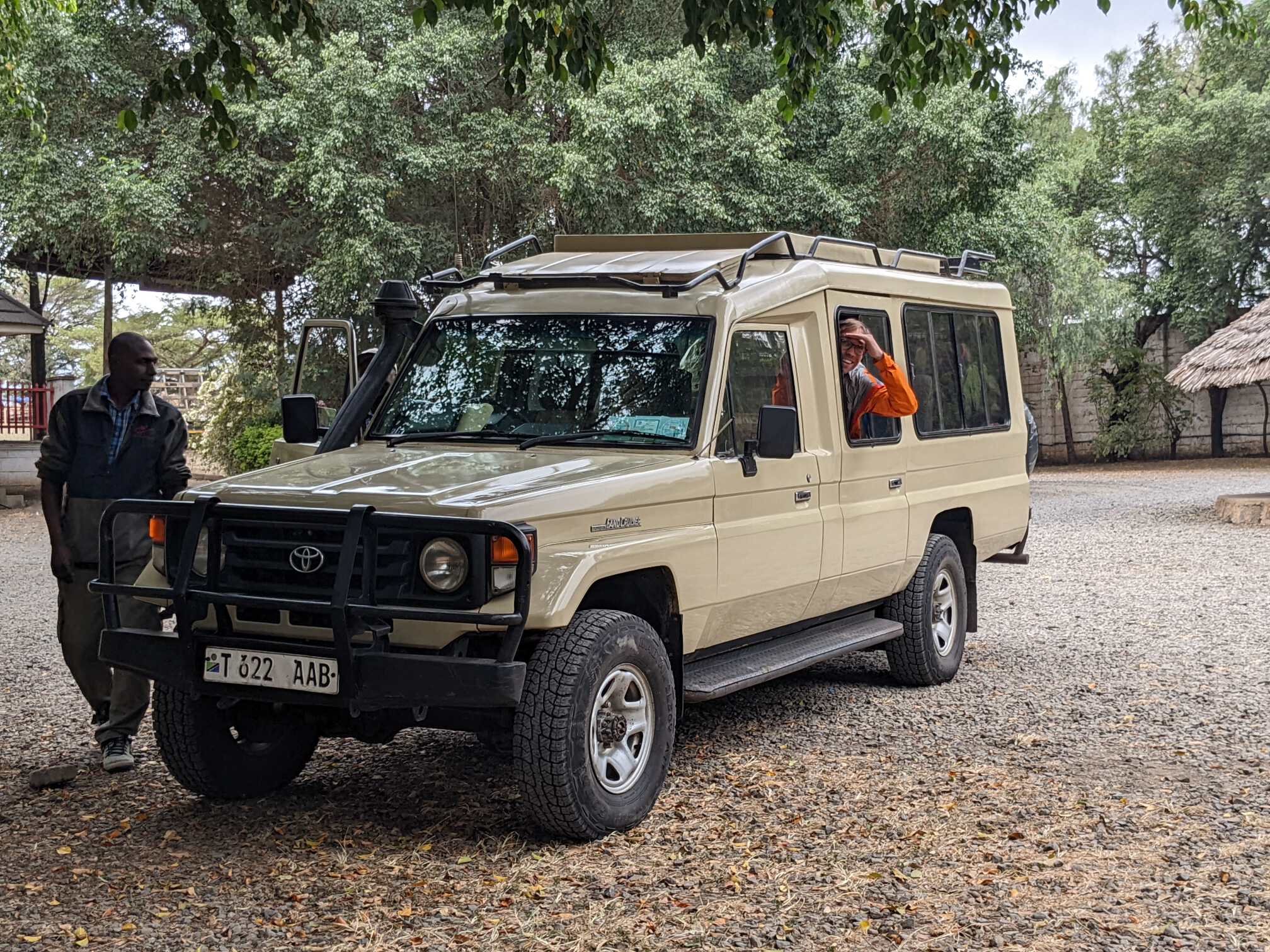 Tim in a neon orange jacket with his hand to his brow to block the sun as he looks out of the window of a sand color Toyota land cruiser